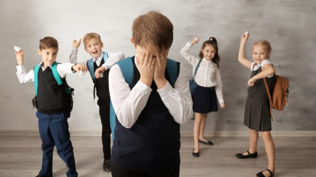 4 crianças jogando papel em um menino, fazendo bullying.